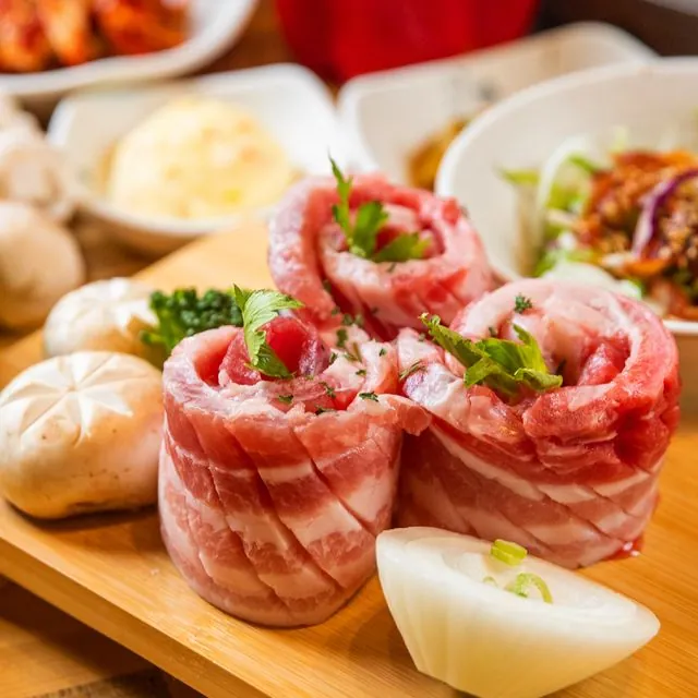 나무 도마 위에 말아 올린 흑돼지 삼겹살과 반찬